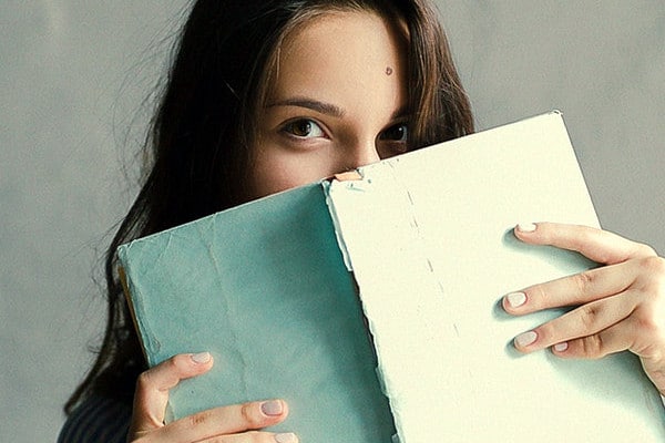 Shy girl holding a book covering her face